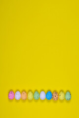 A row of bright Easter eggs on a yellow background. Place for an inscription. View from above.