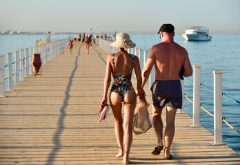 A couple of people walking on a pier in swimsuits watching and snorkeling