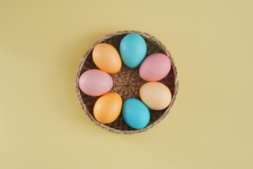 Minimalistic Easter composition on a trendy yellow background of Easter eggs painted in pastel colors in a wicker basket. Top view, flat lay