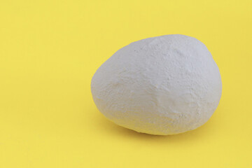 Handmade egg covered with gray plaster on a yellow background. Minimal Easter.