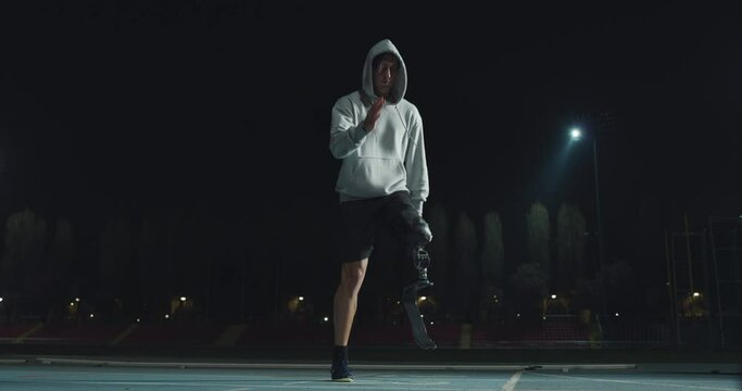 Cinematic shot of disable man with legs prosthesis is warming up before run with dedication on car track at night. Concept of handicapped people active lifestyle, determination, motivation.