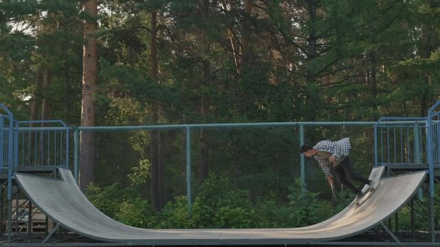 Side view shot of guy skating up and down and doing stalls on half-pipe ramp in skatepark