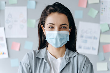 The concept of health, self-defense. Beautiful brunette in a protective mask on the background of the work wall in office.
