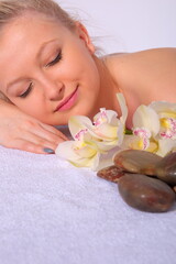 Obraz na płótnie Canvas A young girl relaxes in a spa while lying on her stomach next to orchid flowers and heated stones. Close-up view