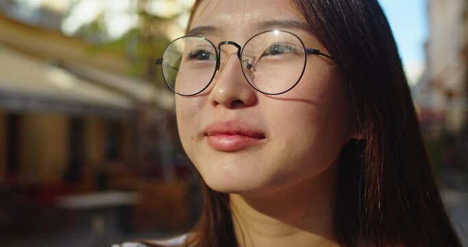 Close up of female face, woman opening her beautiful eyes, while looking at sun. Young Asian lady enjoying warmly sunny day. Cute smile with dimples on cheeks. Summer, life, happiness concept.