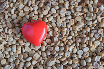 Red heart on a pile of coffee beans on wooden background.