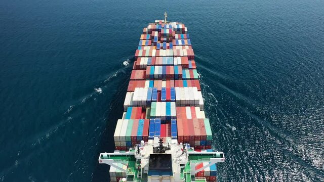 Aerial drone flight above fully loaded container ship cruising open ocean sea for logistics import export, shipping or transportation