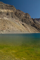 Natural background. View of the yellow shallows, blue water lake, rocky cliffs and mountains, high in the Andes cordillera in Chile.