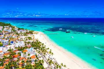 Beach vacation and travel background. Aerial drone view of beautiful atlantic tropical beach with straw umbrellas, palms, boats and pirate ship. Bavaro beach, Punta Cana, Dominican Republic.