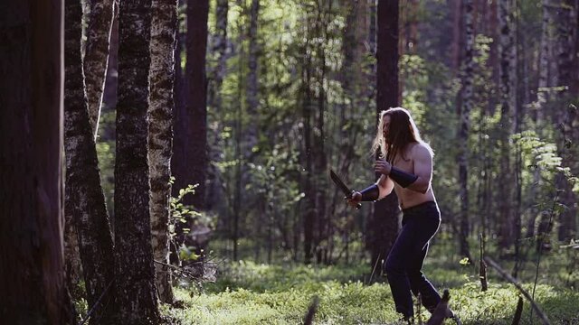 A man in the evening in the forest practices blows with a blade with an imaginary opponent. Cool light and atmosphere