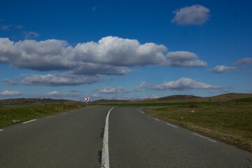 Asphalt road with a white dividing strip going beyond the horizon. Blue sky with fluffy white clouds