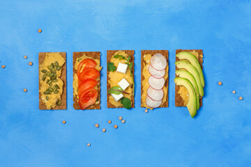 Healthy vegan sandwiches with hummus on rye crackers, with slices of fresh vegetables. Top view on...