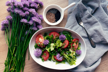Healthy salad in bowl on breakfast on a table with lettuce, tomatoe and flowers of chives. Homemade dish for vegetarian and natural green ingredients. Top view.