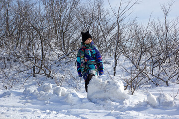 Fototapeta na wymiar The child rolls a ball of snow. Winter fun outdoors
