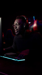 A cute black man plays an online game in a computer club and uses a headset to communicate with the team