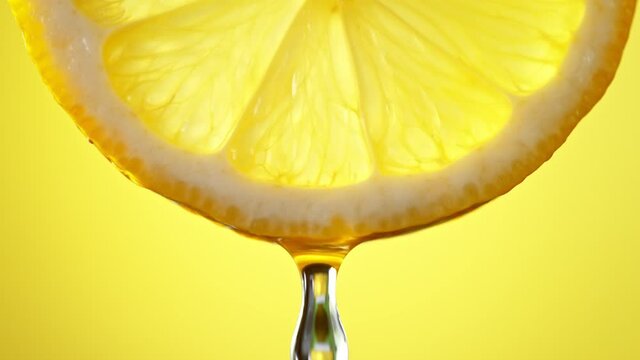 Super Slow Motion Macro Shot of Water Drop Falling from Lemon Slice on Yellow Background at 1000fps.