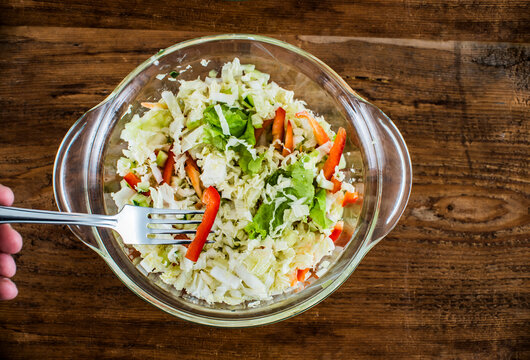 salad made from green gabbage and red paprica stand on wooden table. metal fork in male fingers