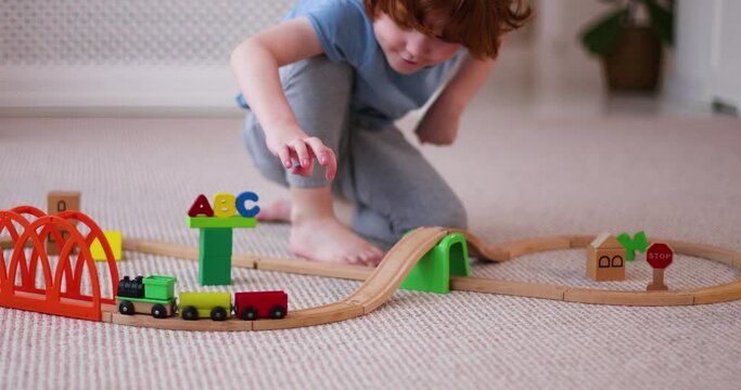 happy kid playing with wooden train on toy railway road at home
