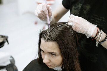 Fototapeta premium process of coloring the hair and painting over the gray hair of a young woman in a beauty salon