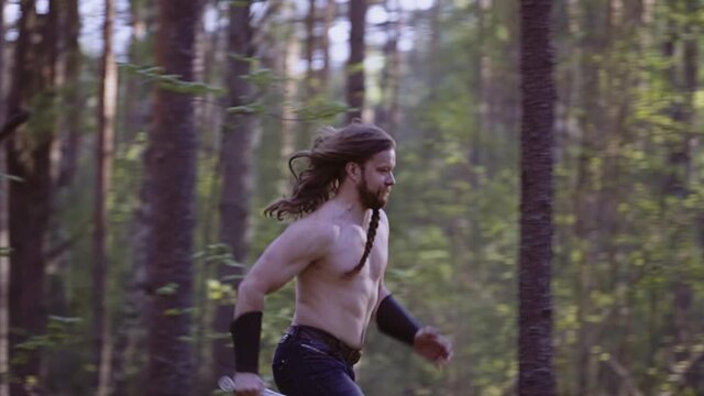 A man armed with a knife runs through the forest running past the trees. Shooting a hero in slow motion