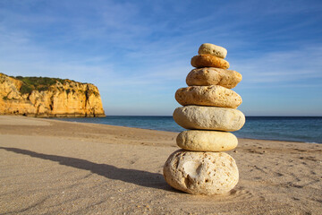 Fototapeta na wymiar pile of pebbles on a sandy beach with cliff, balance, zen concept