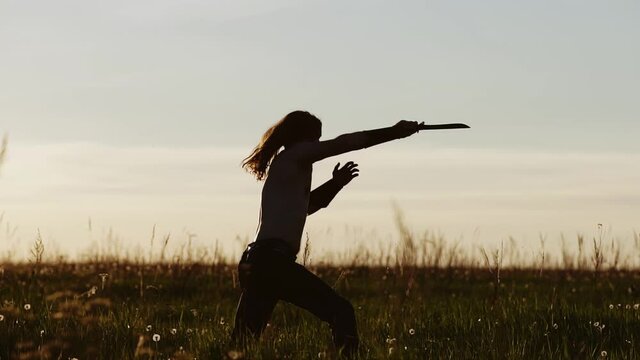 A fighter with a knife, long hair and a bare torso stabs an imaginary opponent with a knife. Slow motion shots at sunset