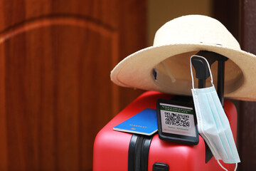 New normal concept. Close up view of a smartphone with an immune digital health passport, a red suitcase, protective mask, straw hat, passport and sunglasses. Traveling by plane during a pandemic.