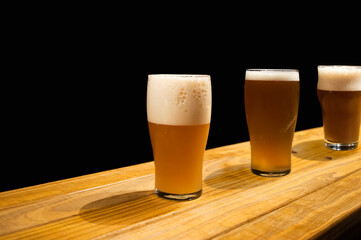 Three glasses of craft beer variations on a wooden surface and a dark background.