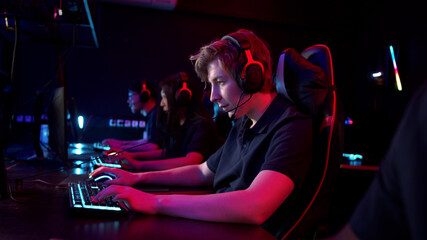 Multi-racial teammates sit in their gaming seats, put on headsets and communicate on them © iaginzburg