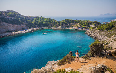 Fototapeta na wymiar Anthony Quinn Bay, Faliraki, Rhodes, Greece. Girl looking at beautiful beach with clear blue water from mountain