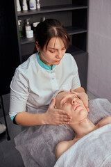 Obraz na płótnie Canvas A brunette cosmetologist gives a facial massage to a young man. Beauty salon. Professional skin care.