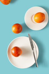 Still life of red oranges on white plates and a table knife on a blue background