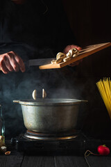 The chef prepares soup on the background of vegetables and spaghetti. Close-up of a cook hand pouring mushrooms into saucepan in a restaurant kitchen