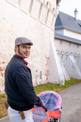 a man in a blue jacket and sideburns walks with a stroller near the wall of an ancient castle