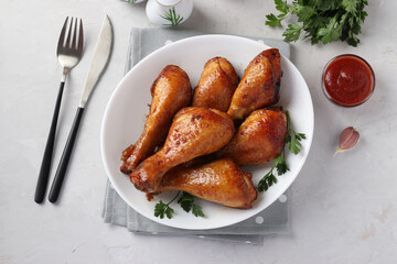 Baked chicken drumsticks in honey and soy sauce on white plate on light background. Closeup. Top view