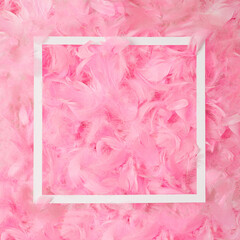 A square white frame with pink feathers in background. Arrangment flat lay. Creative copy space.