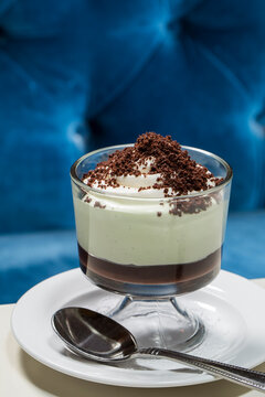 Grasshopper Icebox Cake topped with chocolate crumbles, served in a glass on a white plate with a silver spoon at a diner booth with blue velvet seat