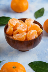 Clementine Mandarin slices in wooden bowl on blue background