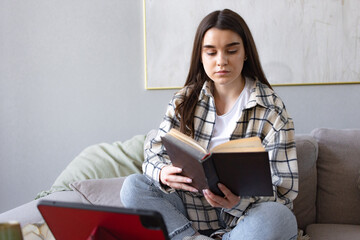 girl reading book, doing homework using tablet