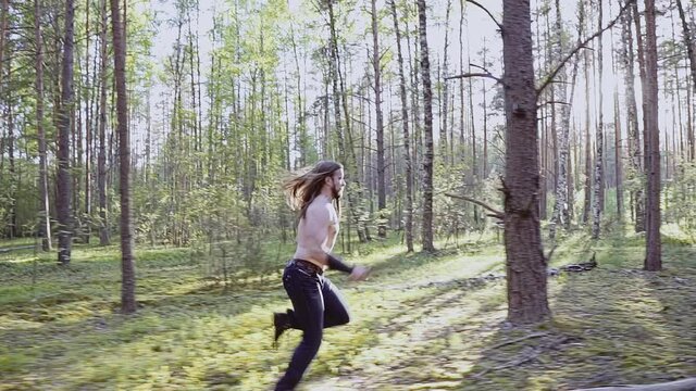 The camera follows a guy who runs with a blade in his hand through the forest among the trees. Dynamic frames