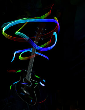 silhouette of an acoustic guitar in the dark illuminated with trails of colored light, painting with light, colored lights, long exposure, vertical