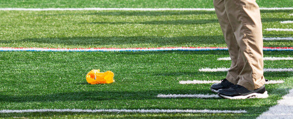Football officials yellow flag on the ground in front of coaches feet