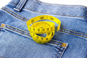 A yellow tape measure for measuring the size of clothes, lies on a blue jeans.