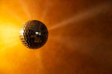 Golden disco ball with light rays on orange background with space for text.