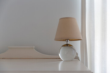 Close up of a small lamp standing on wooden decorative table next to the curtain.