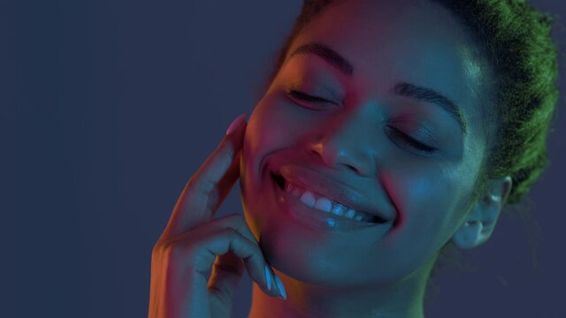 Beauty care. Charming young african american lady stroking her smooth face and smiling to camera in neon lights