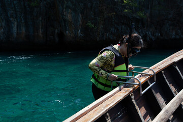 A female tourist wearing a snorkel and a lifeboat is taking the boat ladder.
