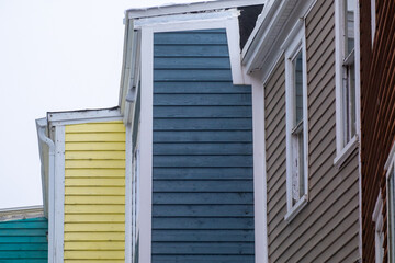 The top corners of five wooden buildings or houses in a step formation. All the buildings have bright coloured wood horizontal clapboard siding with double hung windows and white trim under a grey sky