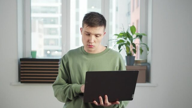 A man stands in an empty room with a laptop in his hands and looks around