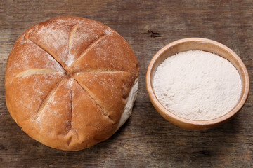 Freshly baked bread loaf round with flour in wooden bowl on rustic wood background